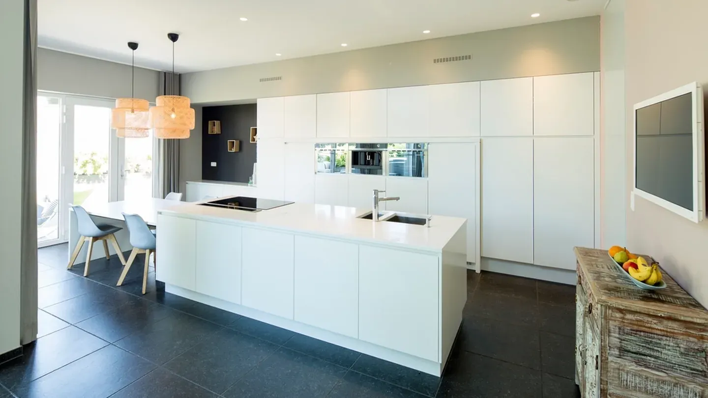 Cuisine minimaliste blanche à façades sans poignées, îlot central et colonnes pleine hauteur